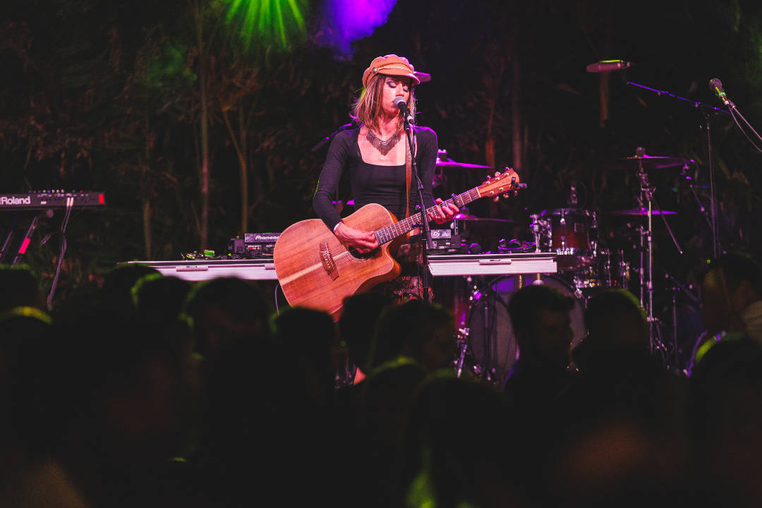 Bella Maree Music girl holding acoustic guitar singing in front of crowd stage lights